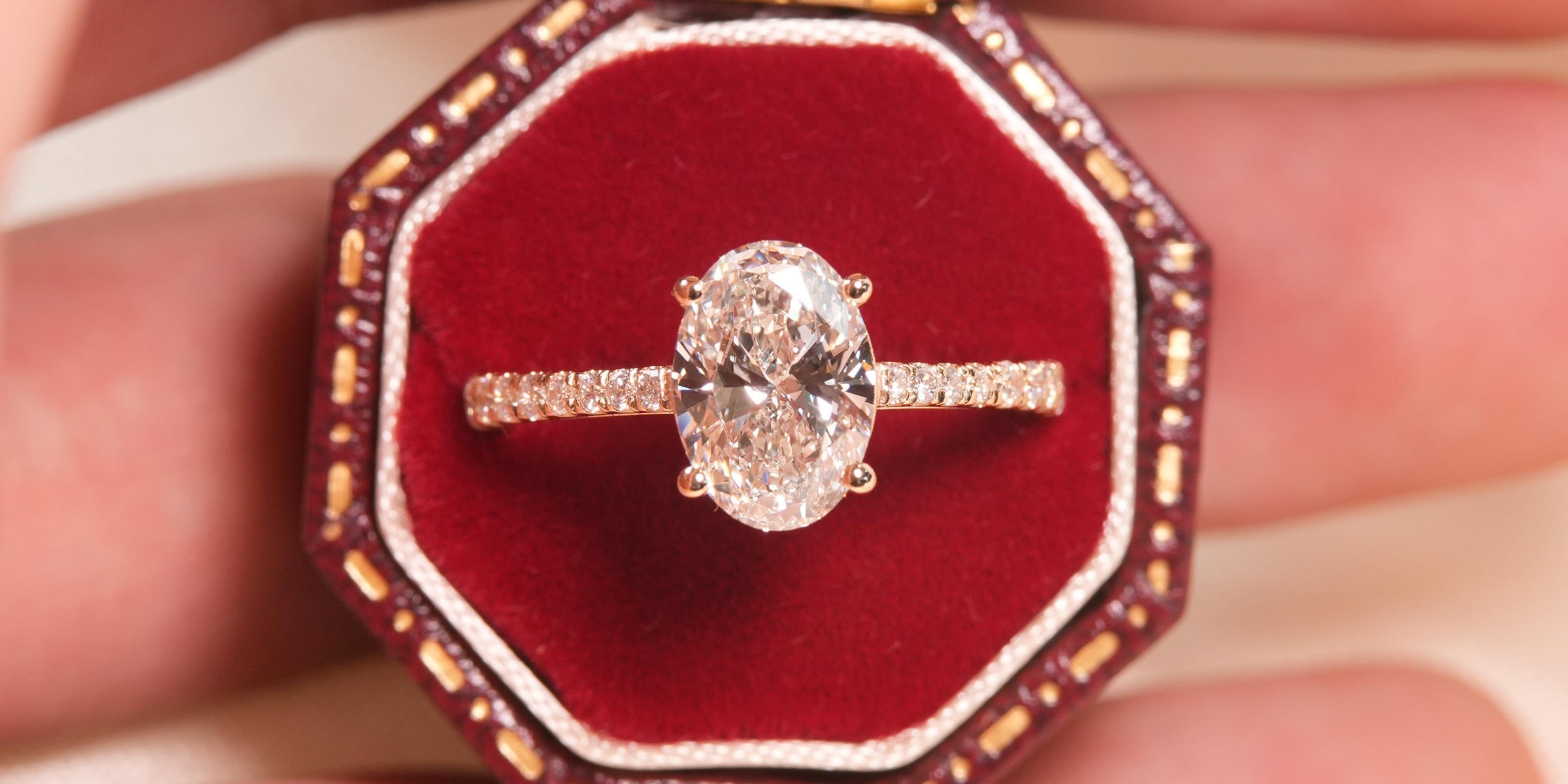 Anel de Noivado com Diamante Natural oval 1 quilate central com aro cravejado em diamantes naturais em ouro 18k amarelo setado em uma caixinha de fundo vermelha.