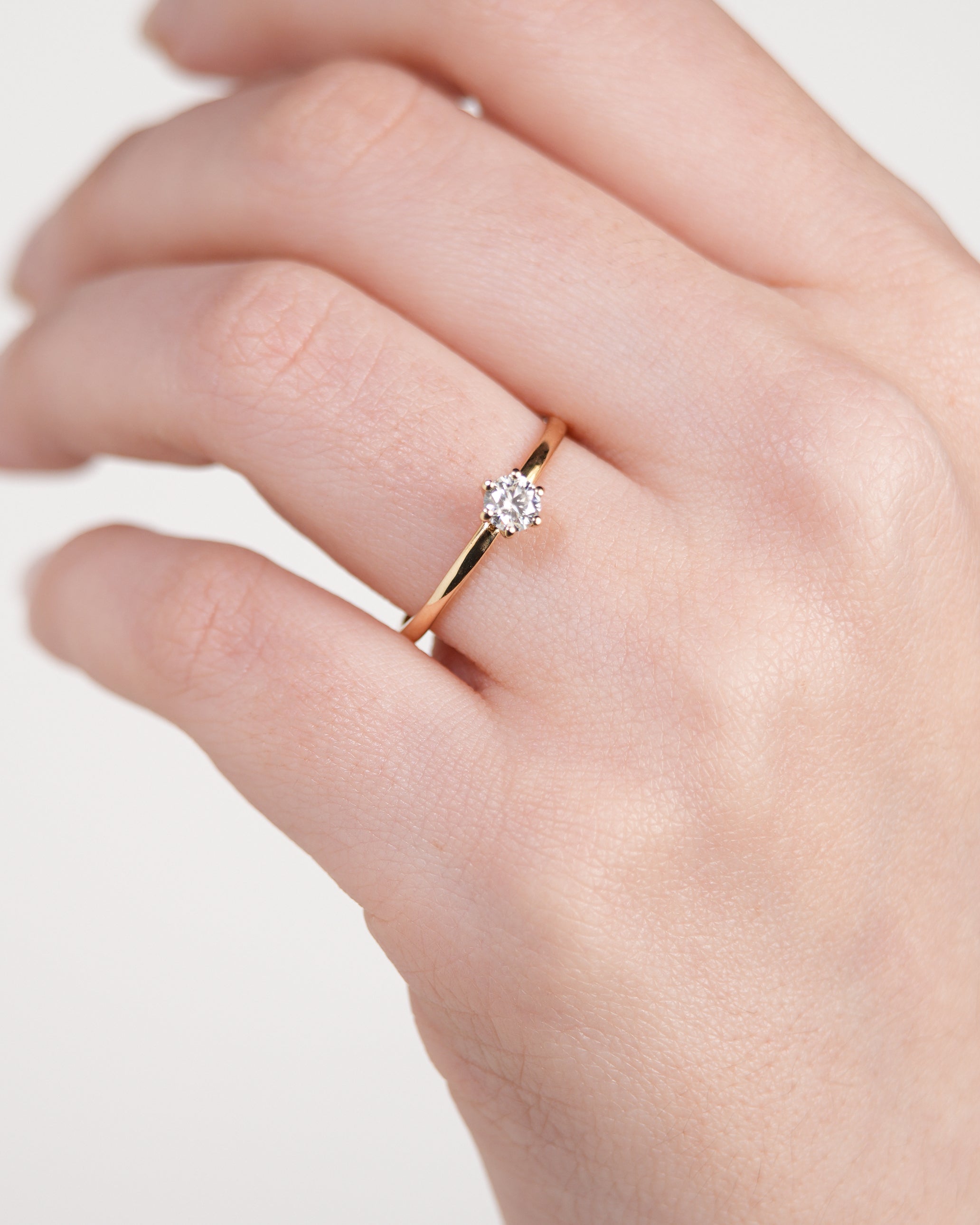 Anel de Noivado Amélie I Solitário em Ouro 18K Amarelo com Moissanite de 0,25ct (4mm) em uma mão branca.