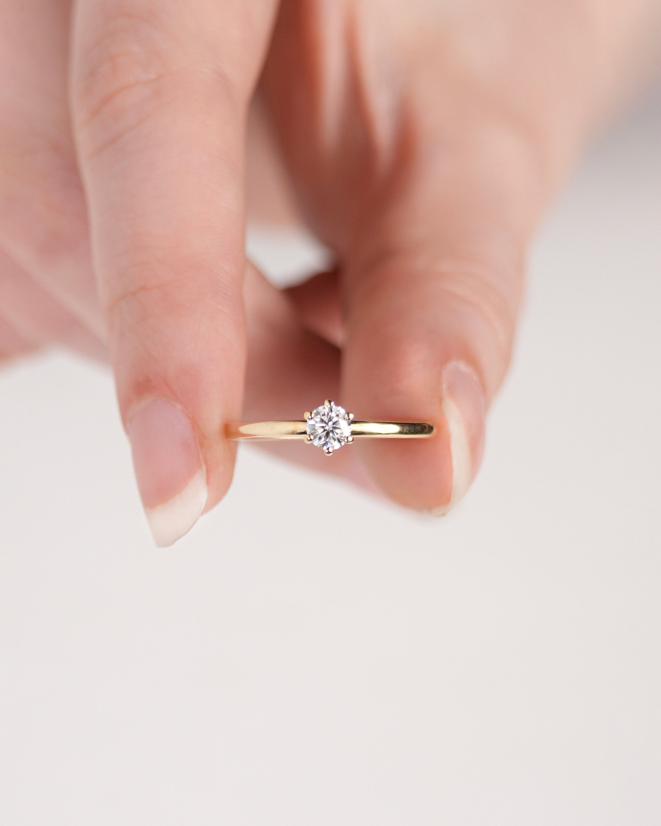 Anel de Noivado Amélie I Solitário em Ouro 18K Amarelo com Moissanite de 0,25ct (4mm) centralizado a imagem segurado por uma mão branca.