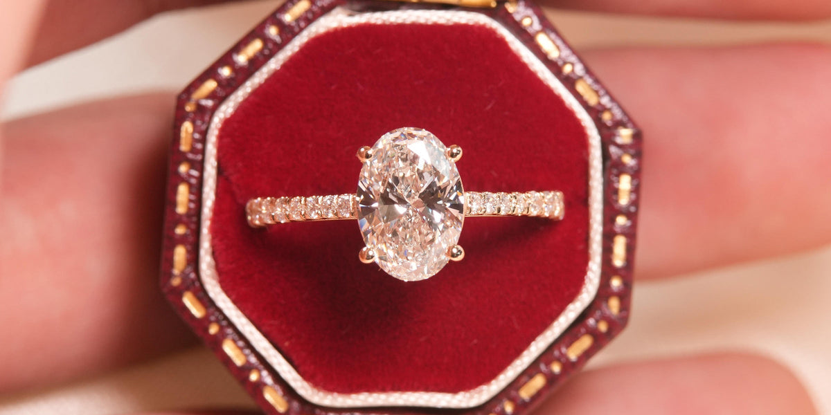 Anel de Noivado com Diamante Natural oval 1 quilate central com aro cravejado em diamantes naturais em ouro 18k amarelo setado em uma caixinha de fundo vermelha. 